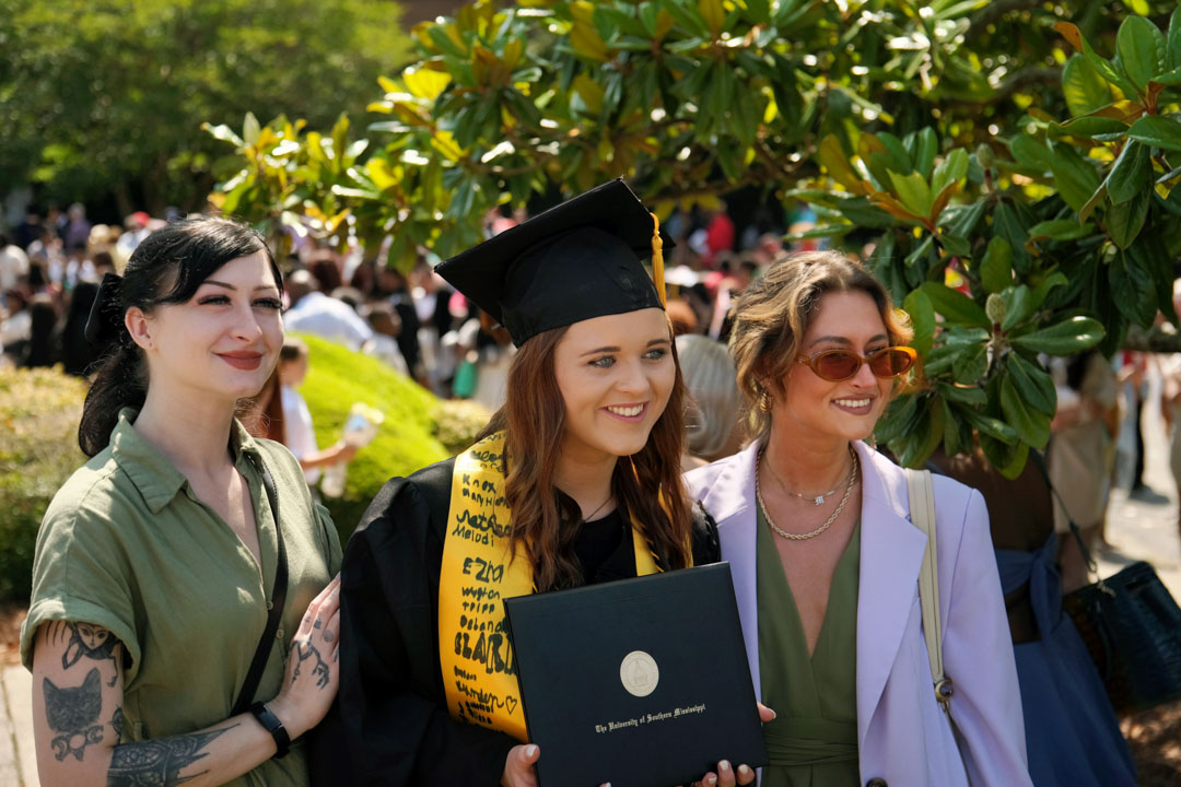 Graduate poses with family and friends outside of Reed Green Coloseum 